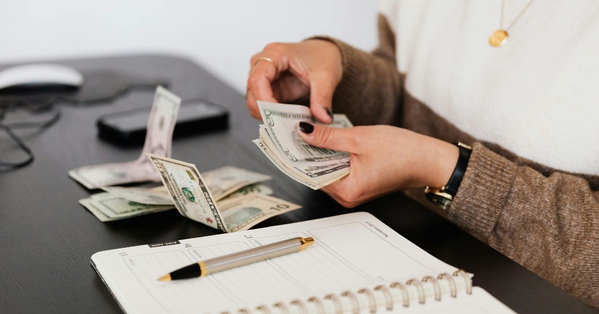 Applying the 50/30/20 rule with dollar bills divided into three sections beside an open notebook.