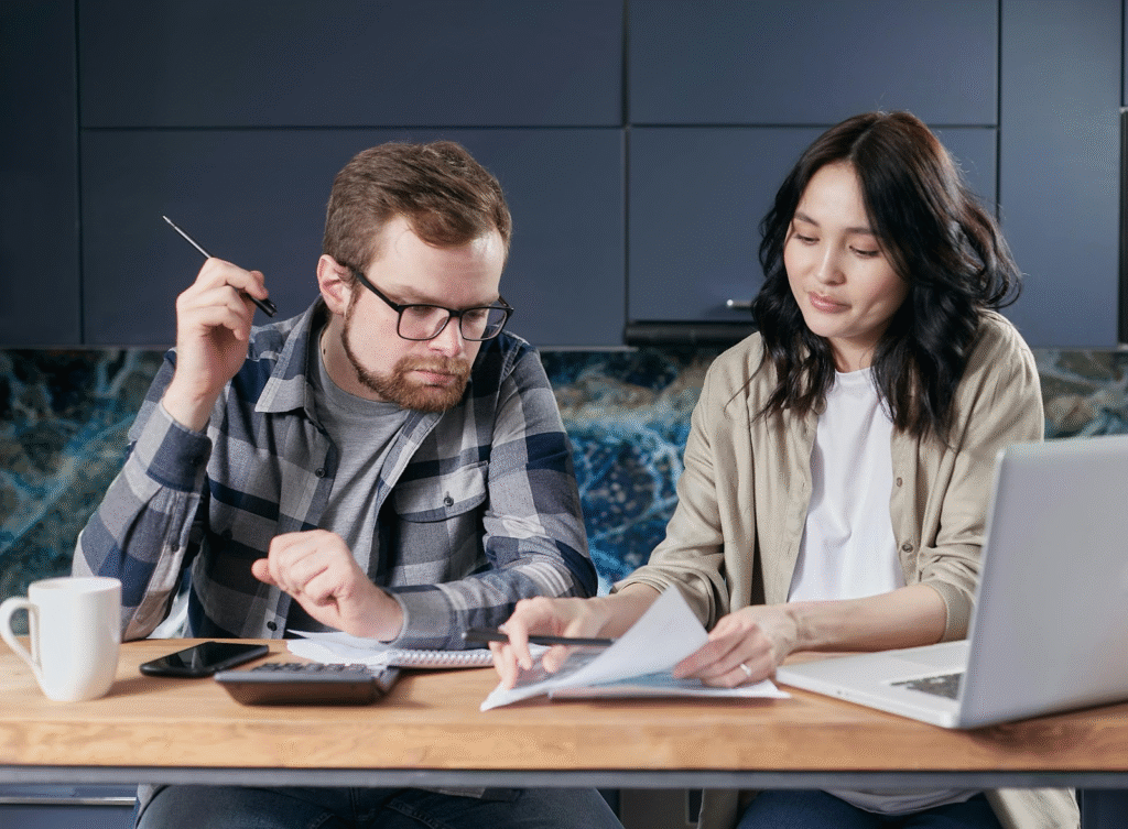 A couple budgeting as a couple while reviewing and calculating their household bills at the table.