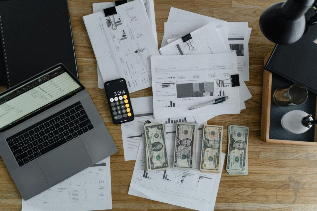 Table with dollars, calculator, laptop, and book illustrating how to build an emergency fund on any budget.