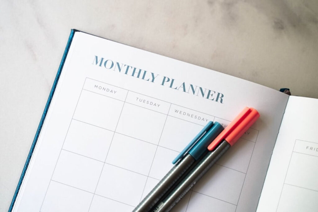 Close-up on an open Monthly Planner with two pens, useful for helping people review their budget monthly.
