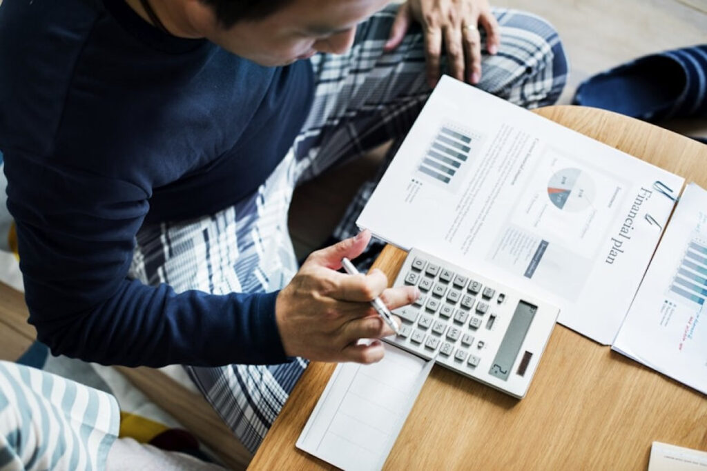 A man calculating finances with a calculator and a document. Likely budgeting using the 70/20/10 rule
