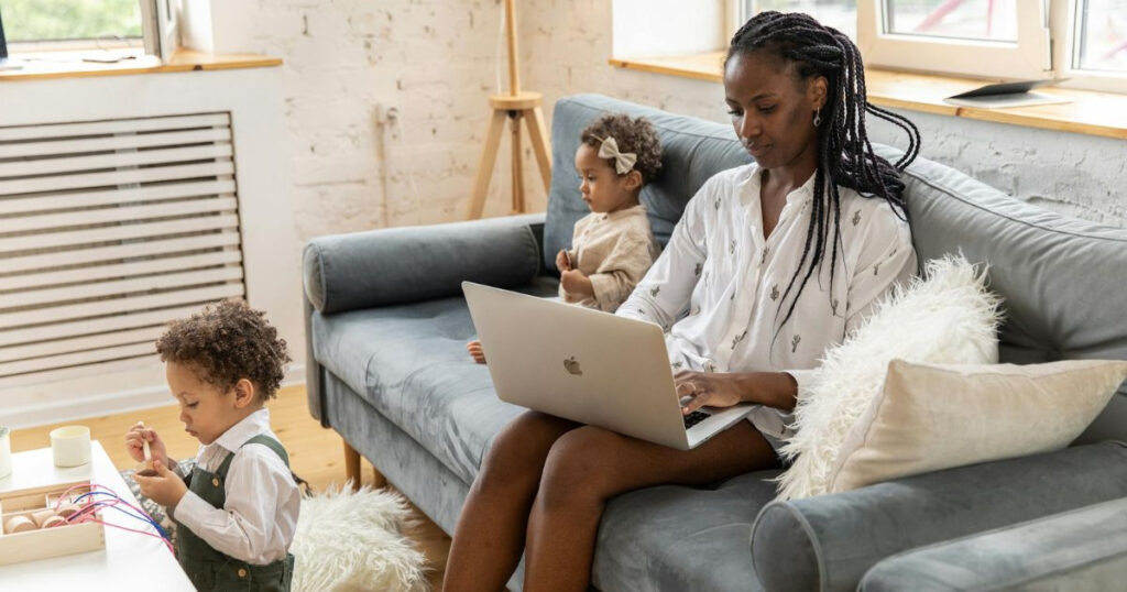 A mom sitting on a couch with her kids while filing taxes as a single mom on her laptop.