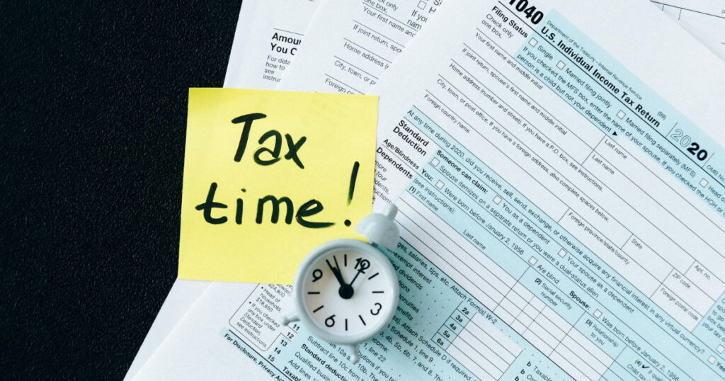 A sticky note reading “Tax time” is placed on a tax form, representing an urgency in filing taxes