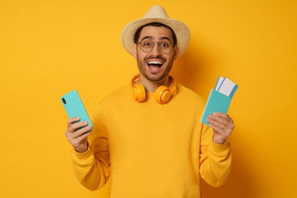 A picture showing a young, excited man holding his passport and tickets in one hand and a smartphone in the other.