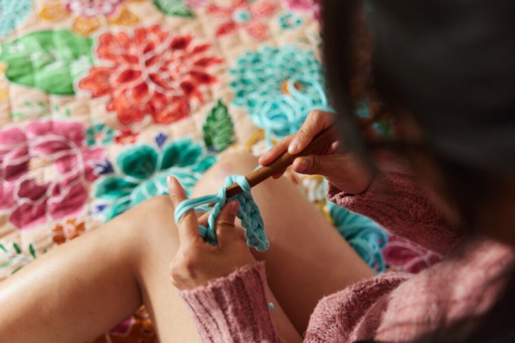 A picture showing a woman knitting a piece of fabric with a crochet hook a perfect gift for celebrating Christmas on a budget