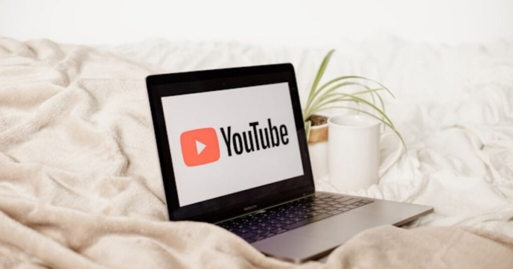 A picture showing a laptop on the bed with YouTube logo on the screen