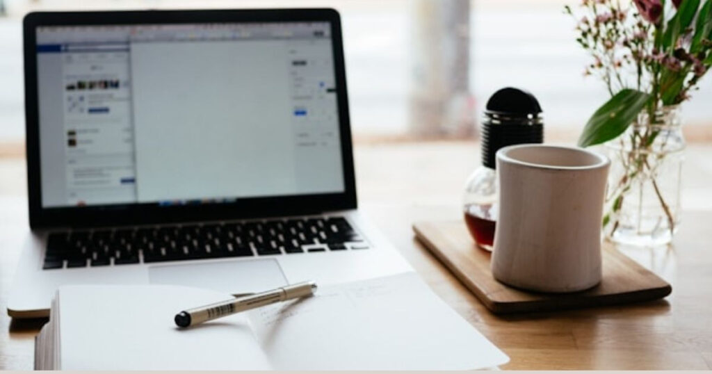 A picture showing a laptop on a table with a mug and a pen