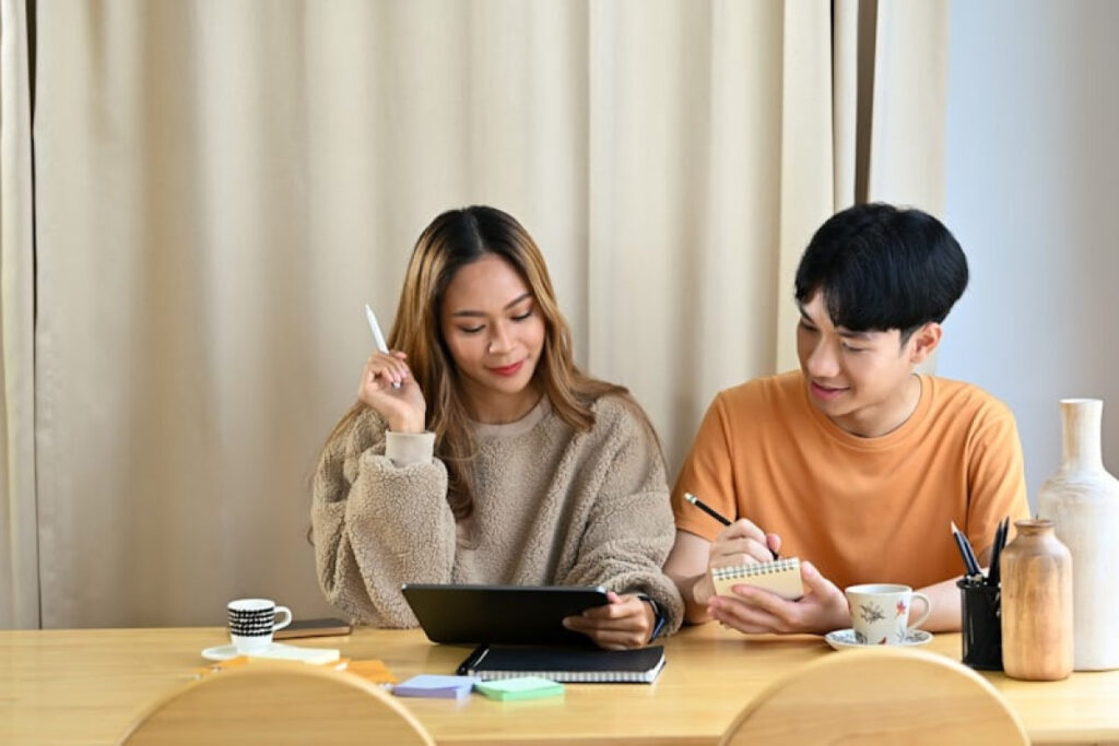 A picture showing a Happy young Asian couple planning how to budget for Christmas as a couple while using a tablet.