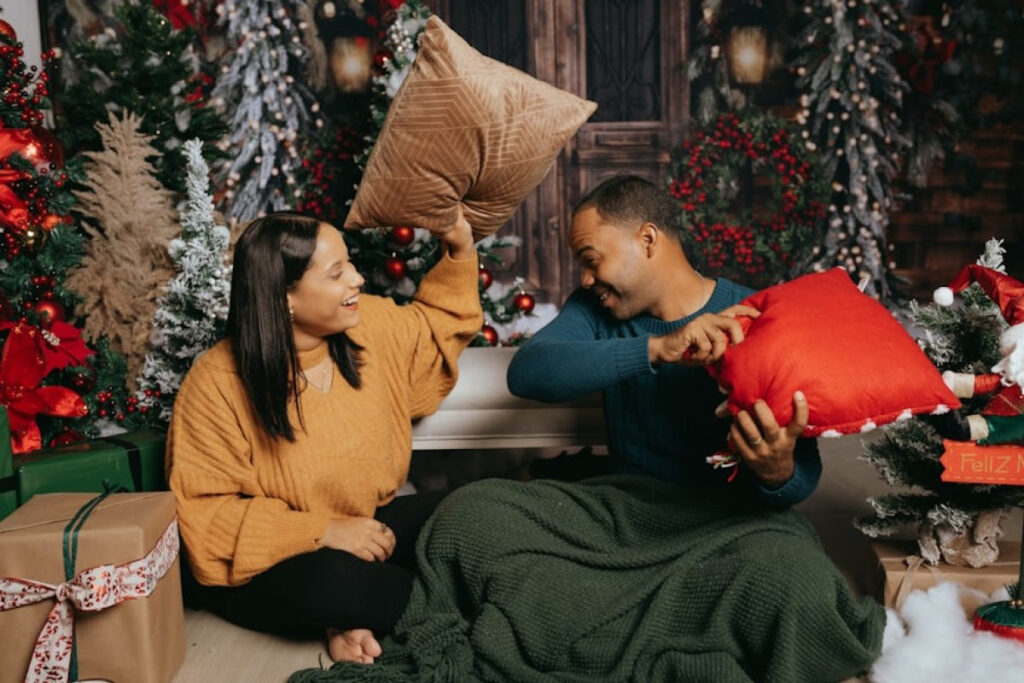A picture showing a couple playfully hitting each other with pillows among Christmas decorations,.