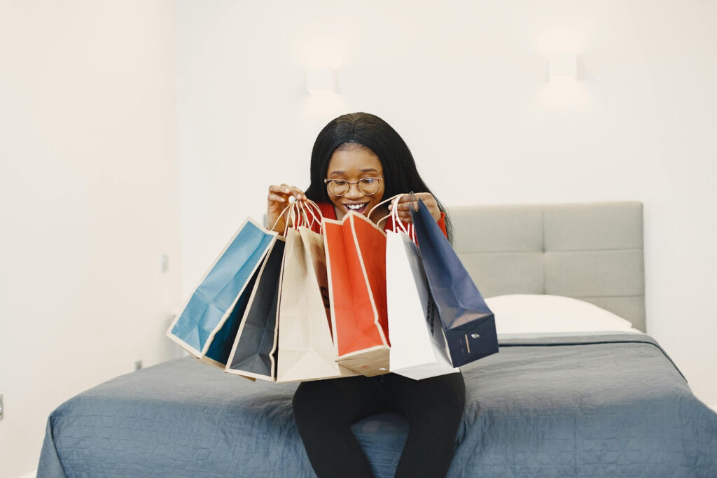 A woman sitting on a bed holding shopped items in paper bags, showing one of the budgeting mistakes to avoid.