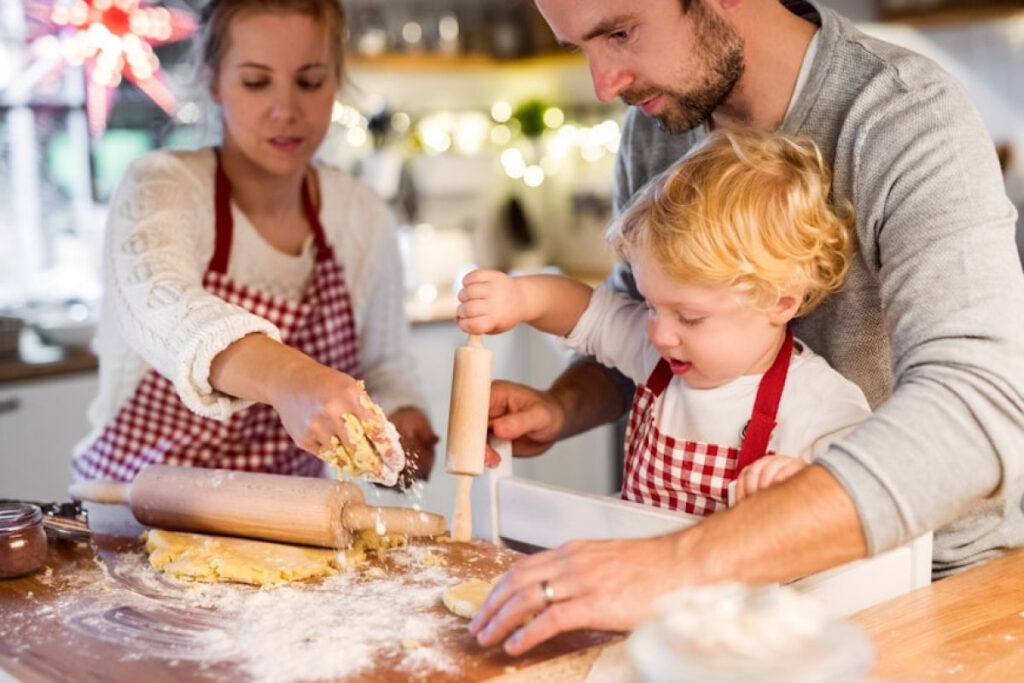 A picture showing a man, a woman, and a toddler boy baking cookies together at home for celebrating Christmas on a budget.