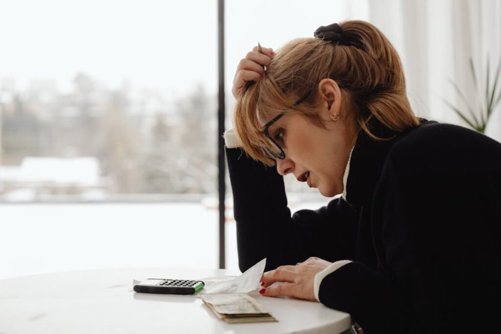 A picture showing a woman sitting at a table calculating debt, reflecting fear and shame