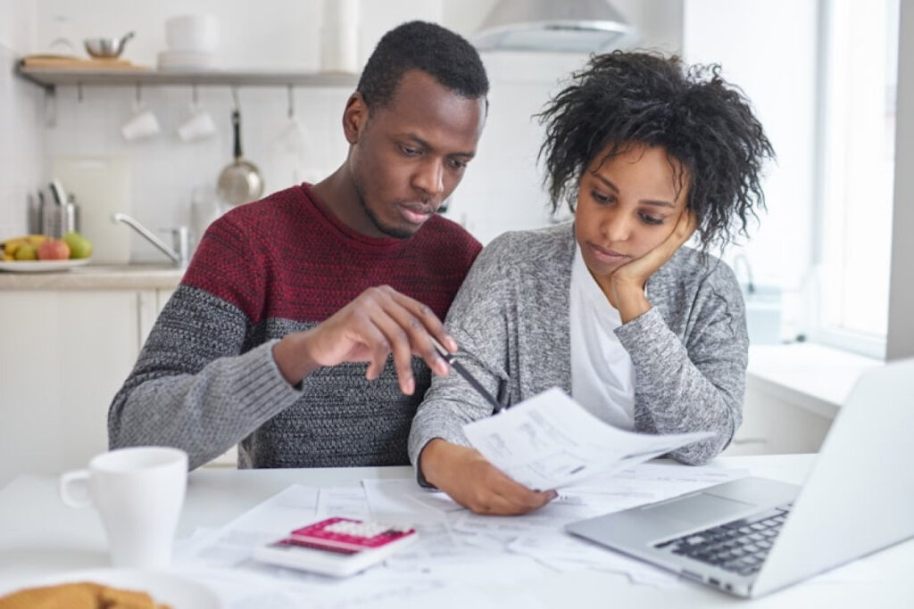 A picture showing : A husband and wife sitting at home with a laptop and calculator, discussing new money rules