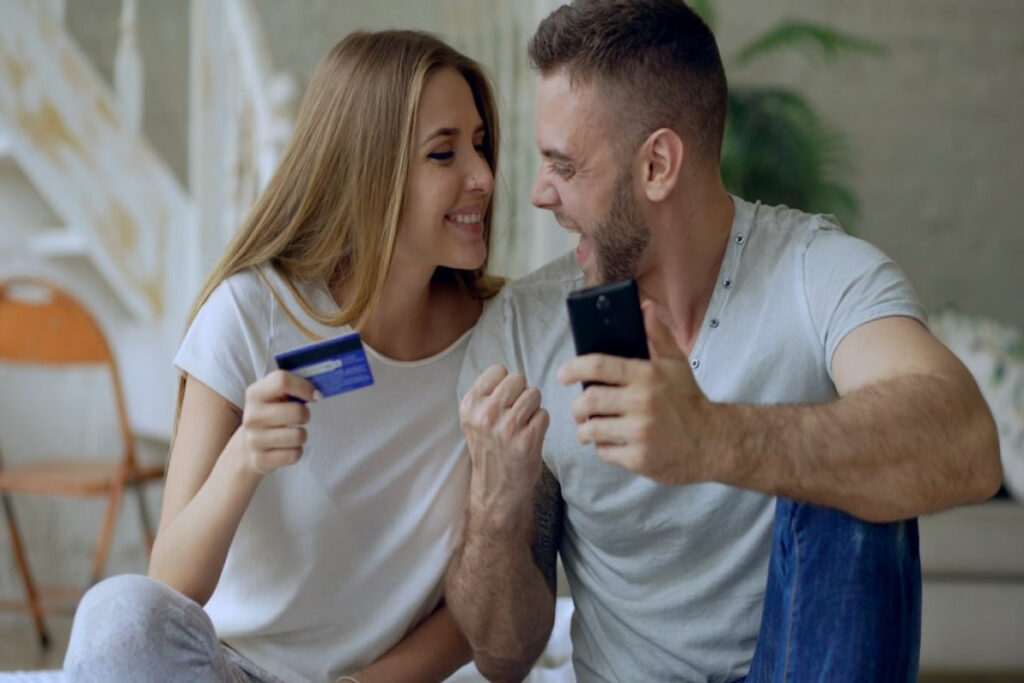 Happy couple shopping online with a credit card and phone, illustrating a joint, separate, or hybrid account setup