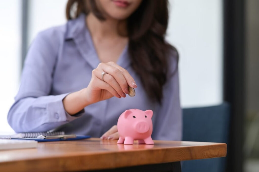 A woman putting a coin into a piggy bank, illustrating saving in a separate account as part of choosing a joint, separate, or hybrid account system.