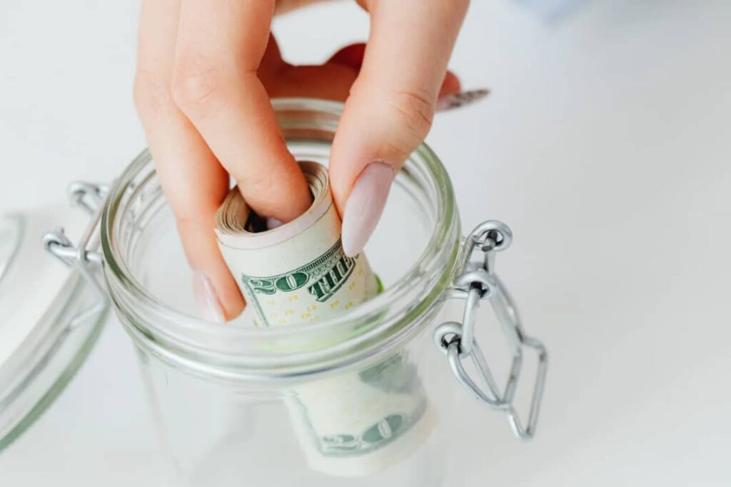 A picture showing someone putting money into a savings jar