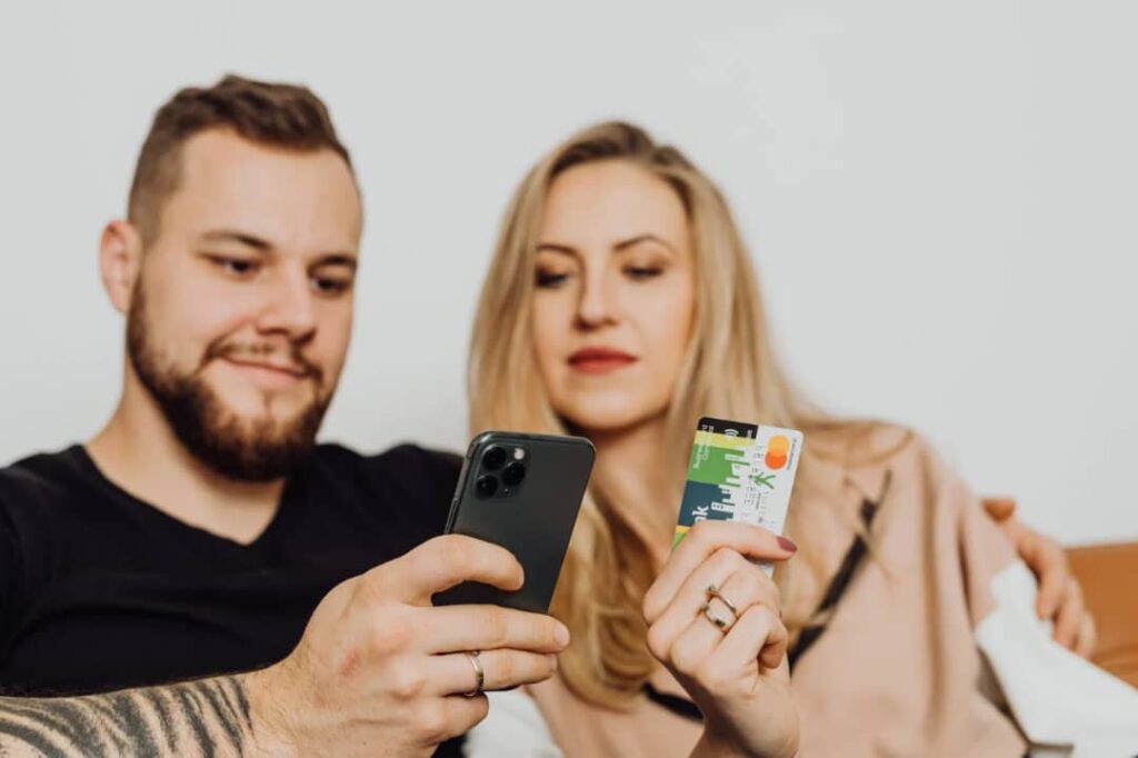 A picture showing a couple with a phone and a debit card, one of the ways of managing money as a couple.