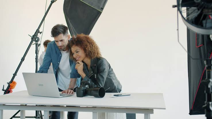 An image showing A couple standing in a photography studio reviewing photos on a laptop. This shows an example of a legitimate side hustle for couples.