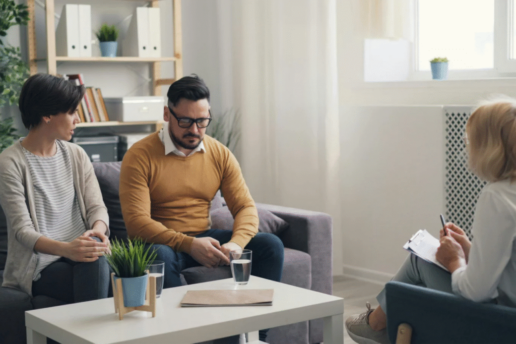 A picture showing A financial advisor talking to a couple at a desk, showing documents and explaining debt repayment strategies, one of the things to do when a partner has a lot of debts