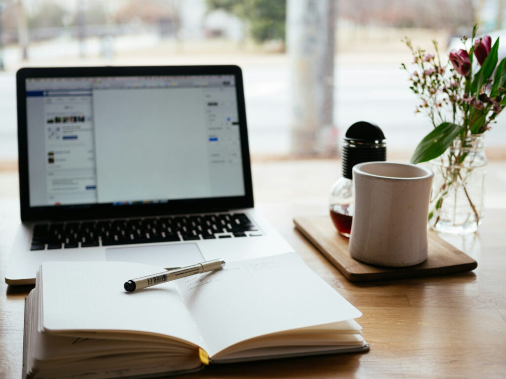 An image showing An open laptop and a book with a mug on a table, illustrating freelance writing as a legitimate side hustle for couples