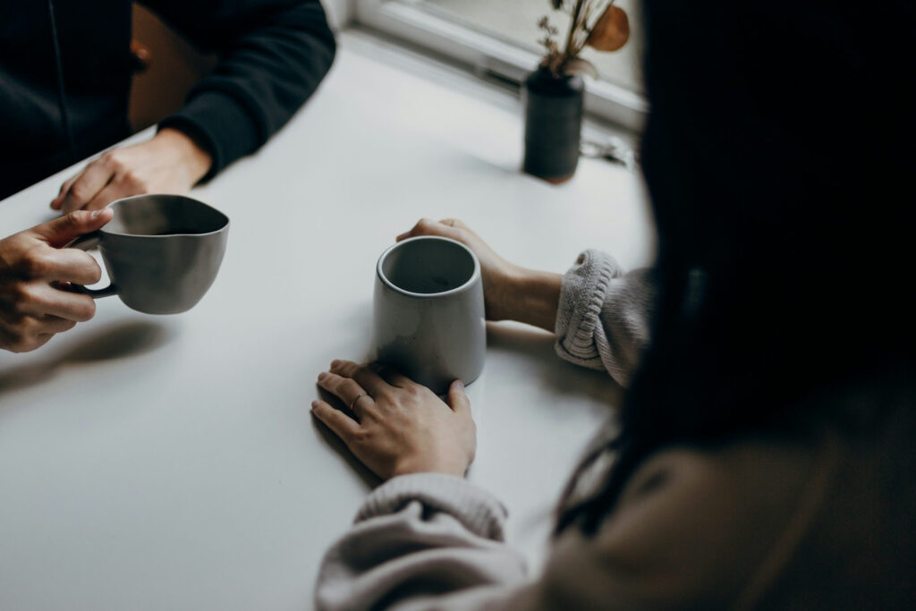 An image showing A couple holding cups while seated across from each other, appearing to converse