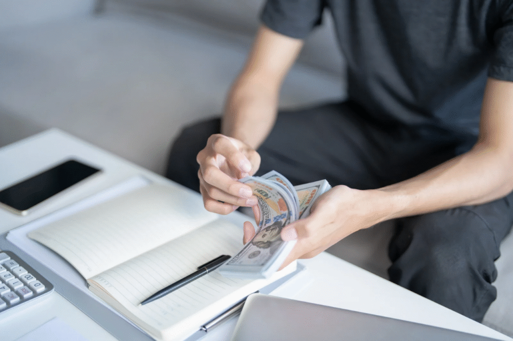 An image showing a man counting money with a calculator and a book
