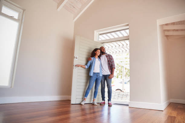 An image showing A happy couple standing in the doorway of a bright, empty room in their new home. They're looking with excitement at a new house, one of the things to do with your tax refund as a couple