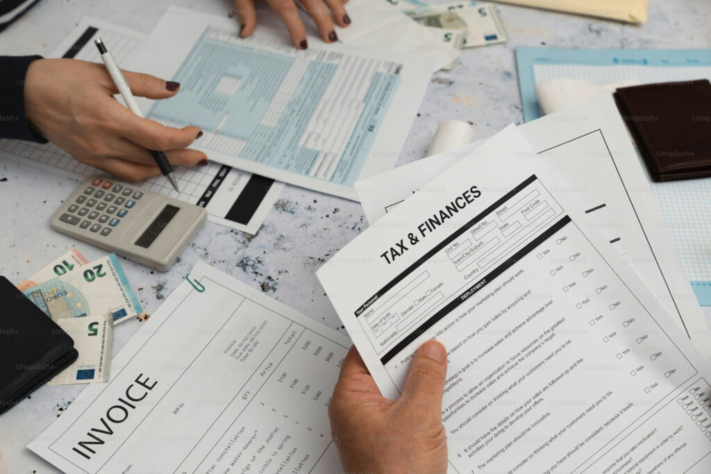 An image showing two hands holding and pointing to tax and finance documents, including an invoice and a calculator, spread across a desk