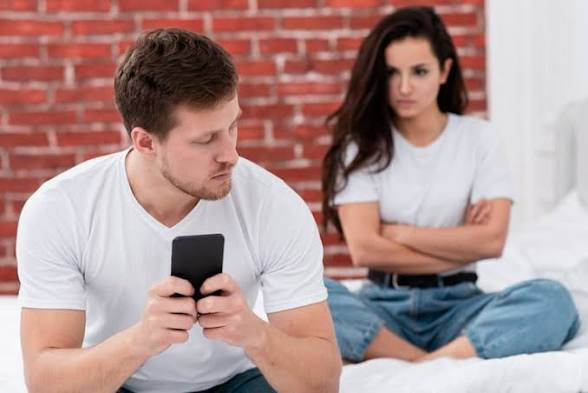 An image showing Alt text: A couple sits close but feels distant. The man is on his phone, while the woman looks frustrated, showing tension from poor financial compatibility in a relationship.