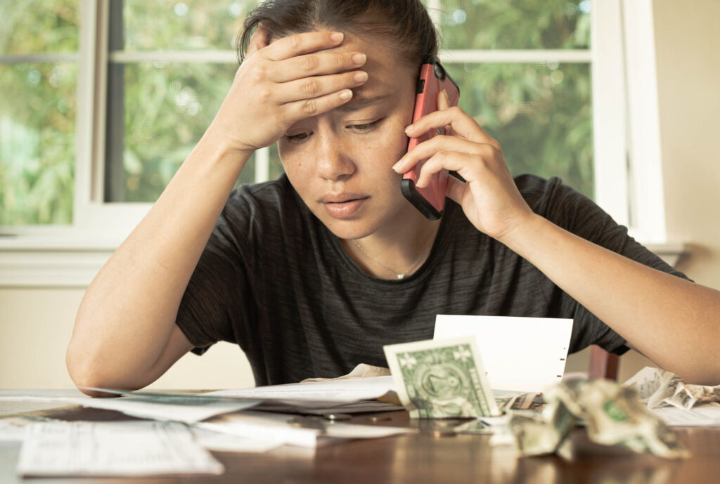 An image shoqing A woman stressed over the financial irresponsibility of her spouse, listening to someone on the phone.