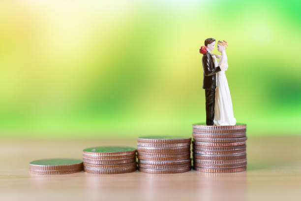An image showing a bride and groom figurines stand atop stacked coins, symbolising financial planning and financial compatibility in a relationship before marriage.