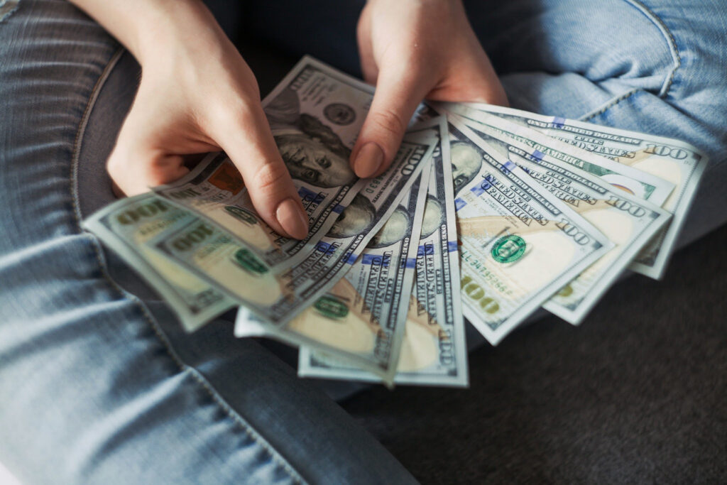 An image of hands spreading US $100 bills over denim jeans, illustrating personal finance and the idea of understanding money language.