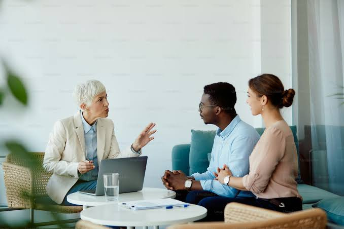 An image showing A financial advisor meeting with a young couple in a modern office to discuss joint financial planning. The scene reflects financial compatibility in a relationship as they work together to align their money goals.