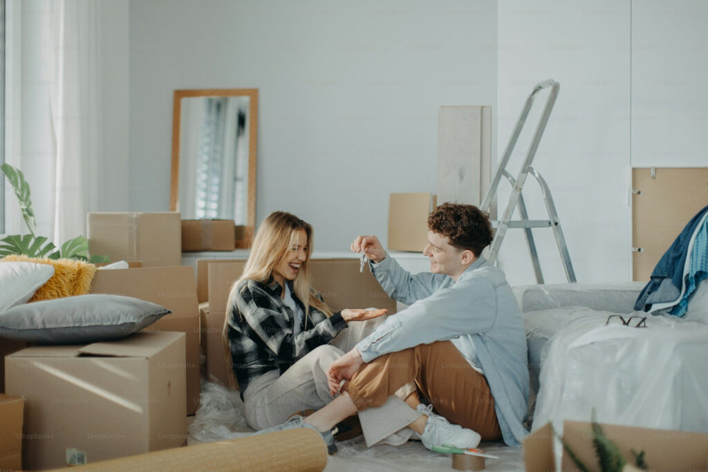  Image showing a Young unmarried couple sitting among moving boxes while discussing homeownership and buying a house before marriage.