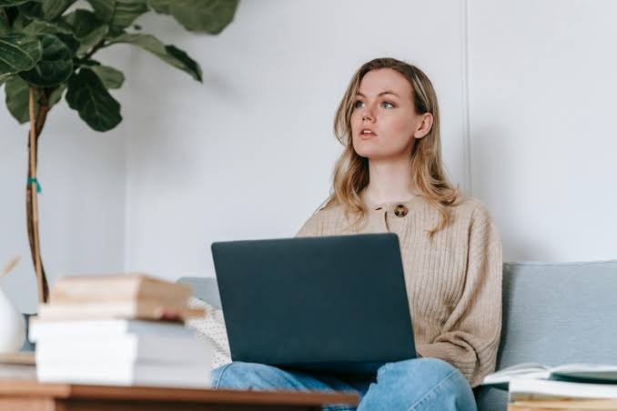An image showing a A woman using a laptop while thinking about financial information related to mortgages, budgeting, and buying a house before marriage.