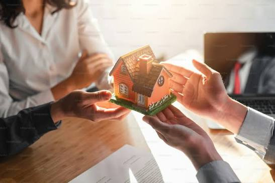 An image showing Couple exchanging a miniature house model during a property discussion, symbolising shared ownership and financial commitment before marriage.