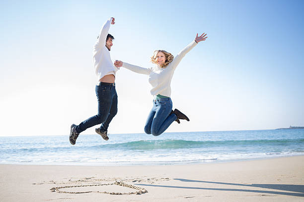 An image showing A happy couple jumping for joy on a sunny beach, celebrating their successful tax refund