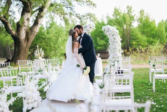 An image showing a Newlywed couple kissing and sharing a romantic moment at an outdoor wedding venue during a beautiful, budget-friendly wedding ceremony.