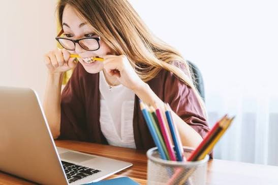 An image showing A stressed female student biting a pencil while looking at her laptop, reflecting the financial pressure many couples experience while trying to pay off student loans as a couple.